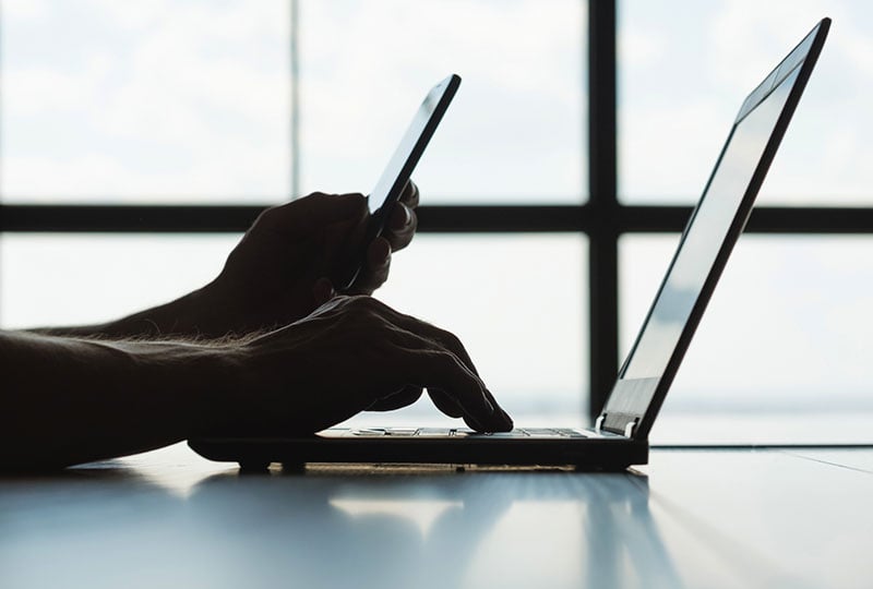image that shows set of hands using a phone and laptop from right