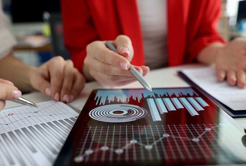 two sets of hands holding pens hovering over paperwork with graphs